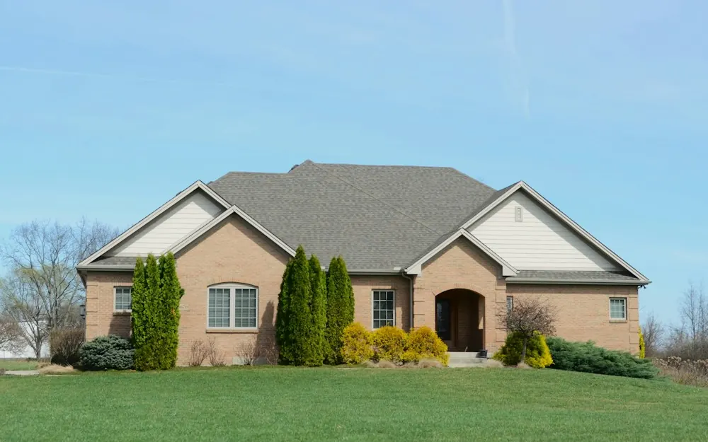 Tan brick single-story home with evergreen shrubs under a blue sky